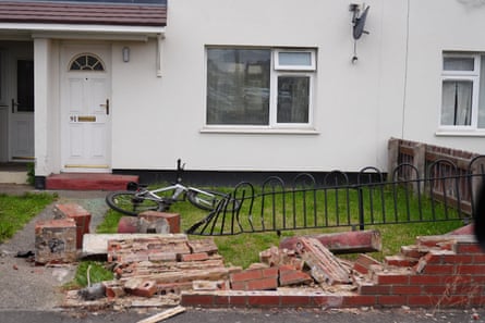 A brick wall has been demolished and black railings buckled in front of a white terrace house with a white front door and green front lawn.