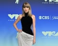 Taylor Swift poses with hand on hip in a black top and sequined skirt