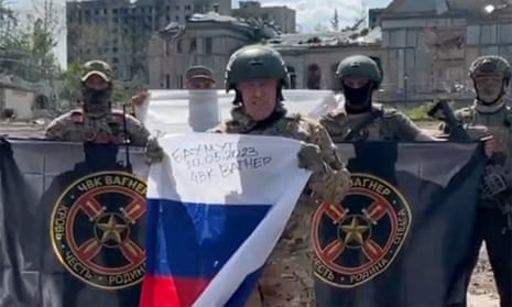 Yevgeny Prigozhin holding a Russian flag in front of armed fighters holding Wagner Group flags in Bakhmut