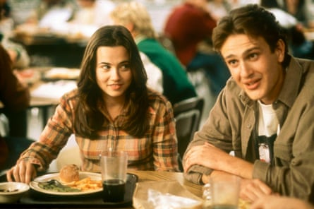 A young woman and man sit at a cafeteria table with trays of food, talking