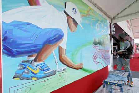 A Black man paints a mural of a Black boy looking into a hopeful scene of cityscape, with outreached hands underneat