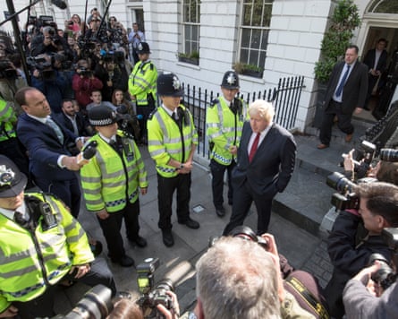 Overhead shot of Boris Johnson leaving his house as police line, photographers and journalists line the streets.