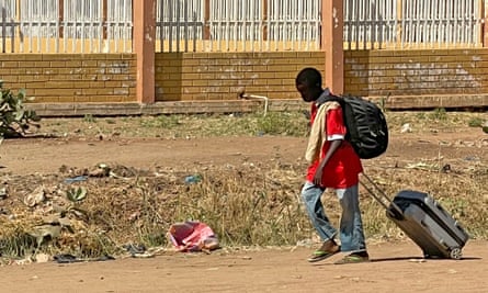 A boy displaced by the conflict in Wad Madani walks with his belongings on a dusty road