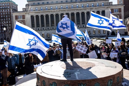 people hold Israeli flags while surrounded by tall buildings