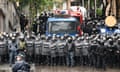 Several lines of riot police stand in front of a vehicle