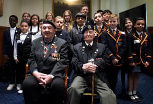 Richard Aldred and Stan Ford wear suits with military medals. They sit in front of a group of children