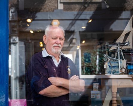 John Spargo stands with his arms crossed in the window of his shop