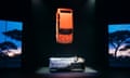 Marc Brew likes in a bed on stage, an orange car, bonnet facing downwards, suspended above him