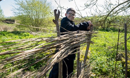 A boy smiling as he builds a prehistoric-style roundhouse with branches