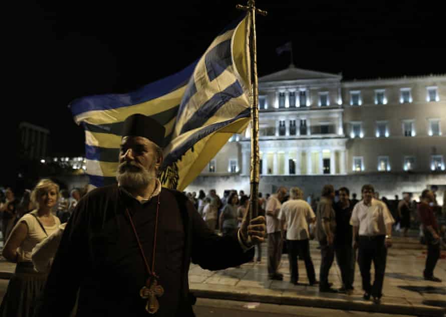 A Greek orthodox priest holds a Greek flag as he takes part in a rally against austerity, supporting the government on the negotiations with its international creditors, in Athens, Greece, 17 June 2015.