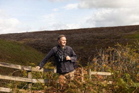 Mark Cocker leaning on a fence in the countryside with his hand on his binoculars.