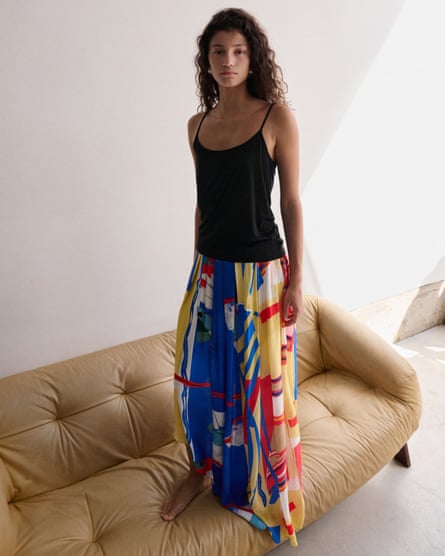 A model stands on top of a cream leather sofa in a black vest and Mango Asymmetrical printed skirt which has a blur red yellow and white abstract pattern