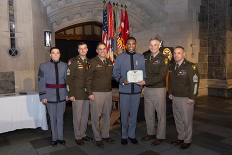 A young cadet holds a commendation surrounded by higher-ranking officers in a hall