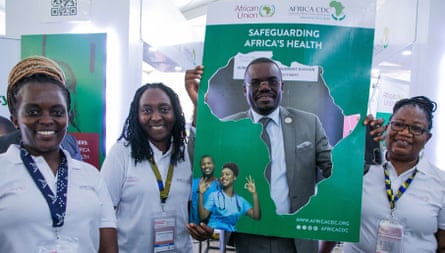 Africa CDC director general Jean Kaseya holds a poster with a silhouette of the continent cut out, and we can see him through the hole. He is flanked by smiling colleagues, all attending a public health conference in Lusaka.
