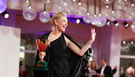 Cate Blanchett poses with the Coppa Volpi for Best Actress award in a dark green dress with a green cape