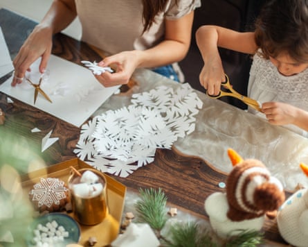 Little cute girl and young beautiful woman cut snowflakes from white paper. Gingerbread and cocoa with marshmallows. The concept of preparation for the New Year and Christmas.