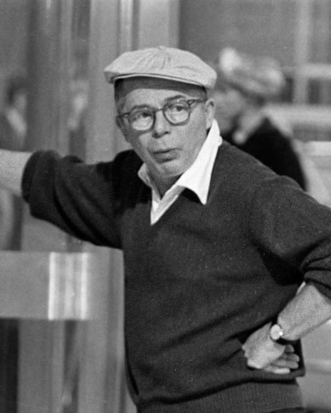 Director Billy Wilder, in glasses and a flat cap, leans on a wall, hand on hip