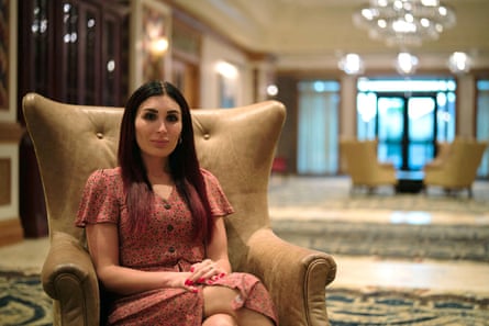 A woman sits in a wingback armchair in a large and luxurious lobby.