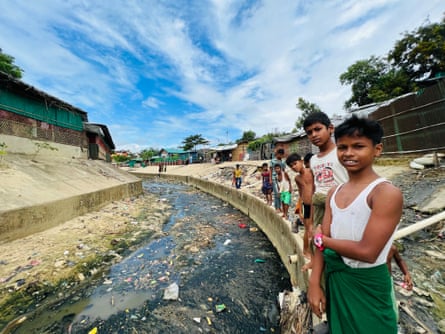 Noen Rohingya-barn går på tomgang ved siden av et concere-dreneringssystem i nærheten av tilfluktsrommene deres designet for å hjelpe til med å kanalisere vann under kraftig regn.