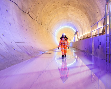a woman in hi-viz suit and helmet walks through a waterlogged concrete HS2 tunnel