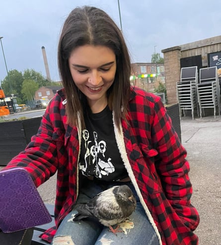 Hannah sits in a pub beer garden, smiling down at a young pigeon in her lap