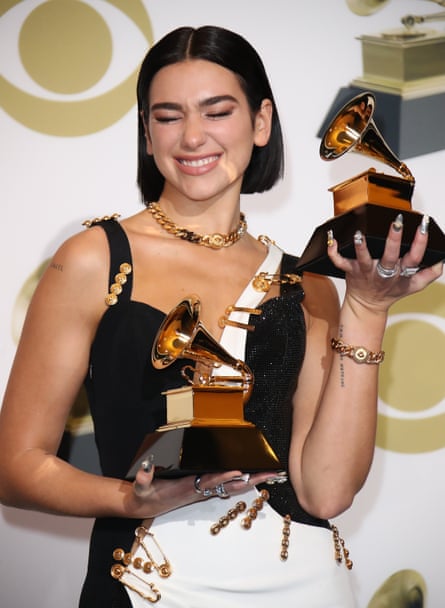 Dua Lipa wearing a black-and-white dress with safety pins and metal details, and holding two Grammy awards