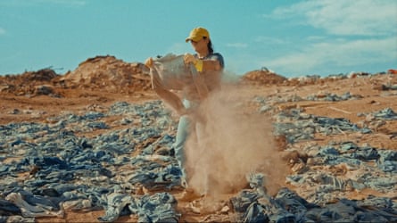 A person in a yellow cap recovers a jacket from piles of clothes in the sand in the Atacama desert