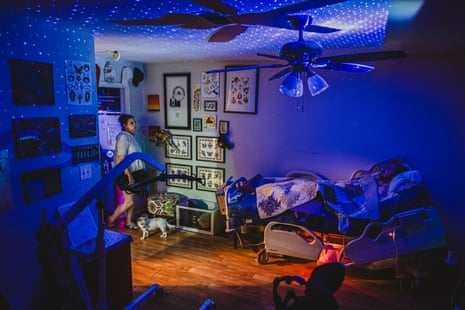 A woman checks on her adult son in bed in a dark room with blue lights and stars