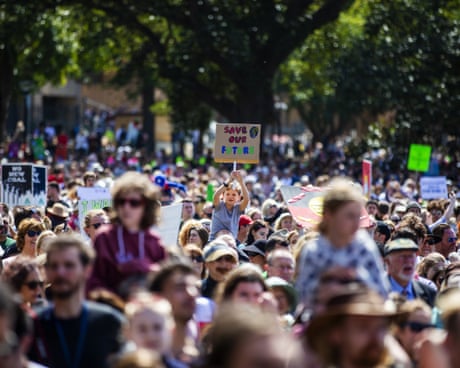 a crowd of people outdoors in front of tall green trees