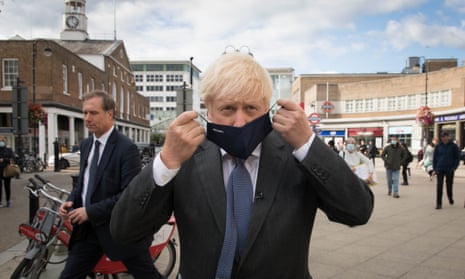 Boris Johnson, close to the camera, put on a face mask as passersby cross behind him in. apublic square