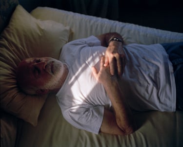 Julian, South Africa, November 2023”I took this photograph of my father during a recent trip to South Africa we took together. He was about to take a nap, but he’s so used to me and my camera that it never seems to bother him. For this shot, I stood on the bed right next to him.I love the creases in his T-shirt, the sheets, and the pillow, and the way the sunlight gently covers his chest and part of his hands. My father is getting older, and his physical health is deteriorating, but in this photograph, he feels calm and strong to me.