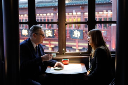 Starmer sits at a table in a window drinking tea, with a Chinese woman sitting opposite him