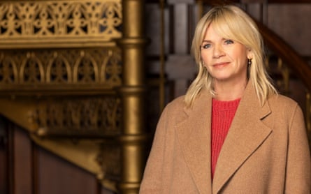 Zoe Ball in a red top and camel-coloured coat with an ornate staircase in the background.