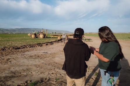 Vasquez in a green shirt hands out a flyer to a person in a black sweatshirt on a farm