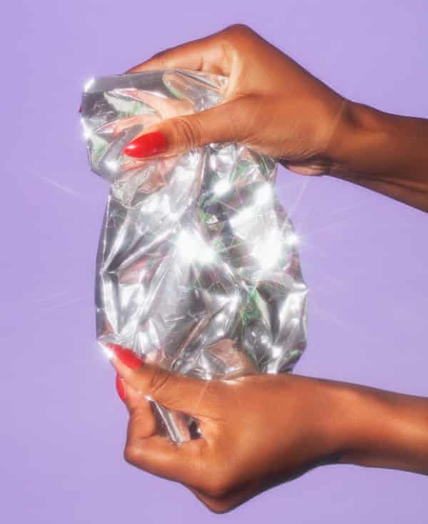 Hands with reddish fingernails clasp a portion of lightly scrunched tin foil