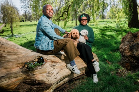 A man and woman sitting on a tree trunk in a park with their dogs