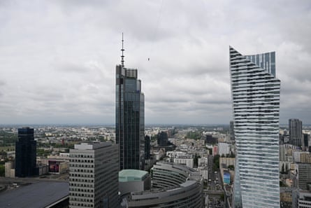 Wideshot of tall buildings with Roose just visible on tightrope