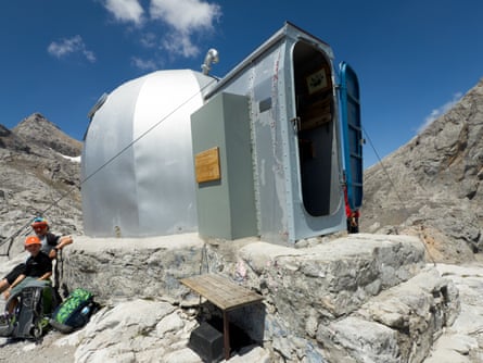 A metal cabin with a doorway and domed section behind, sitting on rocky terrain