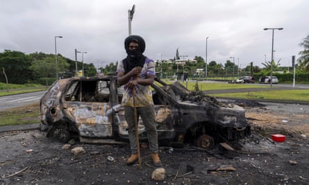 A man stands in front a burnt car after unrest in Noumea, New Caledonia.