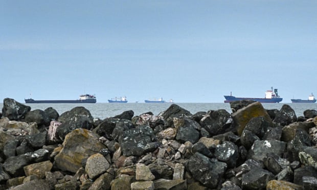 Cargo ships waiting to enter the Sulina canal from the Black Sea stretch in a line along the horizon behind a foreground of rocks