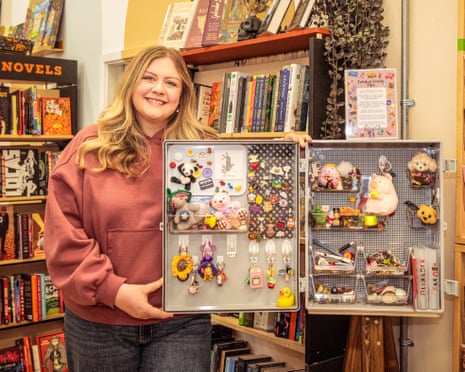 Sam Stevens holding open a box with lots of small toys and trinkets, inside a bookshop