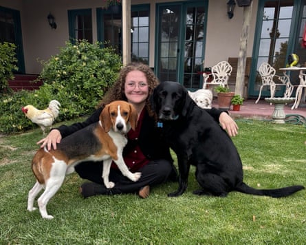 Woman on a green lawn cuddling a beagle on one side and maybe a black lab on the other.