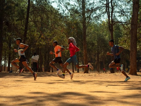 A group of men run on a sandy path next to the treeline.