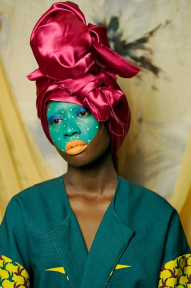 A woman wears teal face paint, orange lips and a large magenta satin headwrap