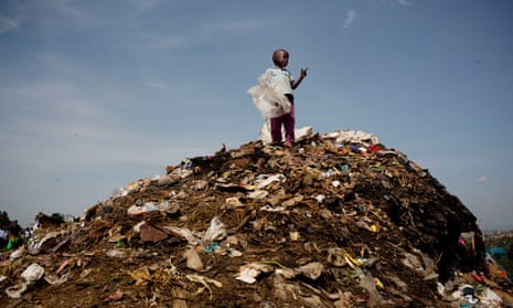 A young boy stands on top of a rubbish dump at the side of the road in Kibera Slum in Nairobi, Kenya 