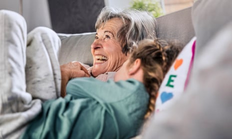 Cheerful grandmother lying by granddaughter on sofa at homeGrossmutter hat Spass mit Enkelin auf Couch im sonnigen Wohnzimmer