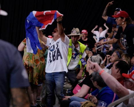 A demonstrator holds a Cuban flag as Donald Trump speaks.