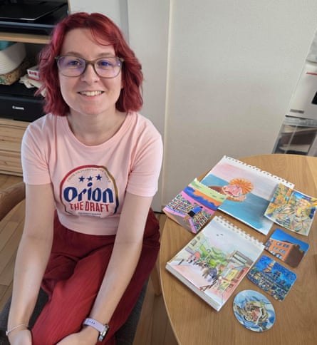 Sarah sits next to a table laden with pieces of her artwork.