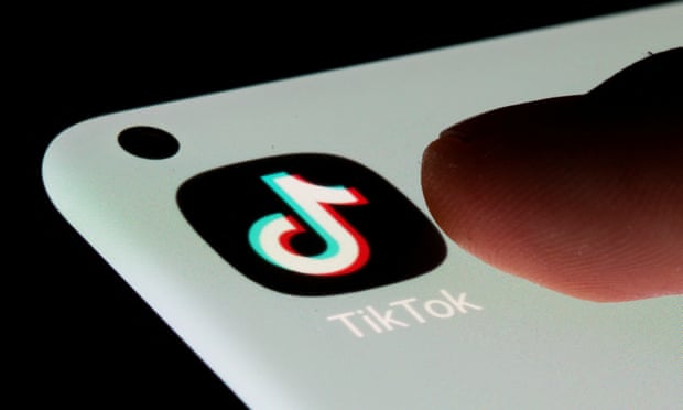 TikTok logo on a phone, with a thumb poised nearby
