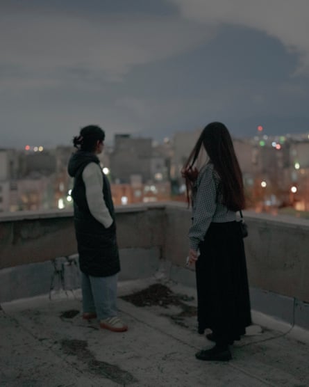 Two women, backs to camera, on a rooftop at dusk looking out over a city